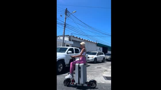 Lady rides scooter while seated on suitcase in Cancún