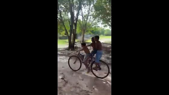 Three boys lose balance on shared bicycle in playful moment in Maranhão, Brazil