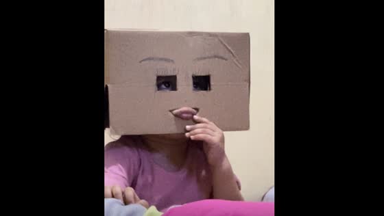 Child wears cardboard with cut-out lips and eyes in video