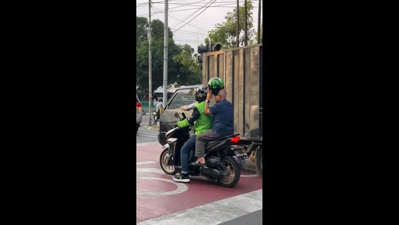 Elderly motorcycle passenger holds helmet instead of wearing it in Jakarta, Indonesia