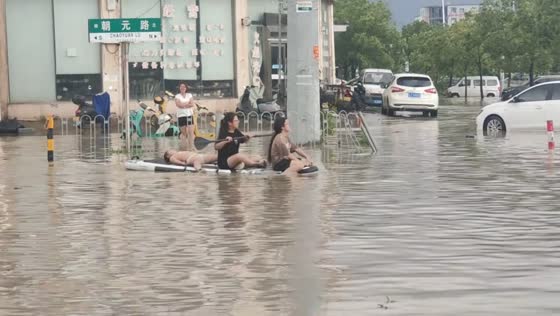 Boy lies on paddle board while riding through flooded street in Taizhou, Zhejiang, China