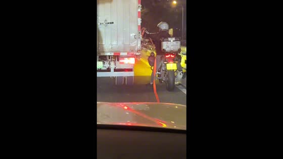 Motorcyclist helps secure a loose cargo strap on a truck in Chongqing, China