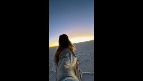 Sunset and moon appear over reflective salt flats in Uyuni, Bolivia