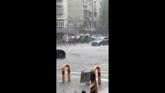 Vehicles drive through flooded street as debris floats in Shandong, China