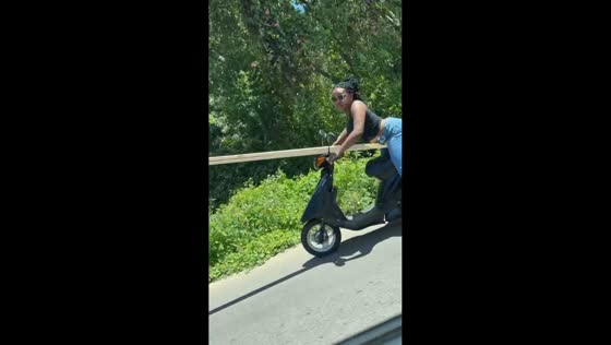 Woman rides motor scooter while carrying wood in Dajabón, Dominican Republic