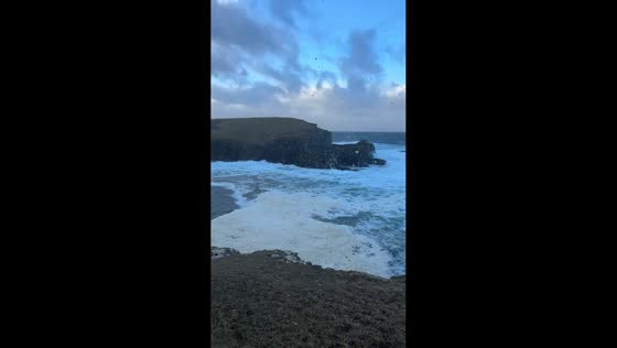 Sea foam lingers along cliffs after storm in Orkney, Scotland, UK