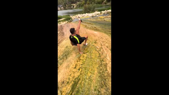Man slips and slides on mossy riverbank in Tivenys, Spain