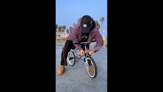 Man rides bike with guitar body and surprises bystanders in Venice Beach, California, USA