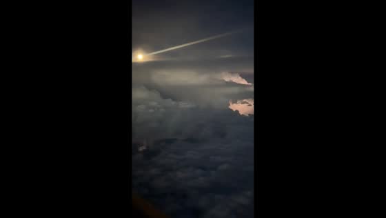 Lightning illuminates thunderstorm beneath full moon from airplane over South Dakota, USA