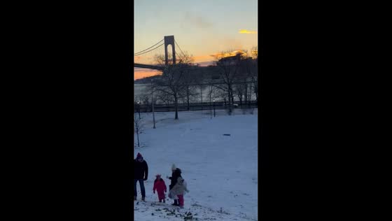 Children sled as cruise ship glides past snowy park in New York, USA
