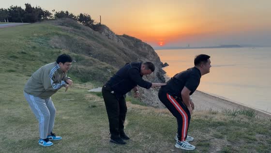 Three brothers perform coordinated gestures by the sea in Shandong, China