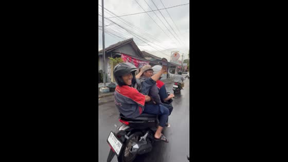 Guy sits uniquely on motorcycle with legs pointing upward in Ngawi, Indonesia