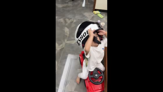 Boy struggles with oversized helmet while riding toy car in Guangdong, China