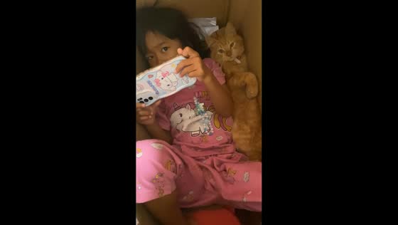 Daughter and pet cat relax together inside a box in Sukabumi, Java, Indonesia