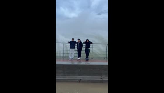 Wave splashes friends at boardwalk in Comodoro Rivadavia, Argentina