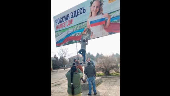 Local residents rip down a Russian poster reading "Russia is here forever" in the town of Belozerki