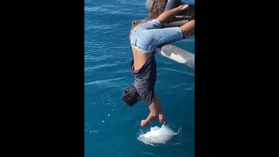 Person catches fish while perched on ship's side in Indonesia