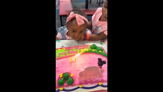 Big sister helps little one blow out birthday candle in Greenville, South Carolina, USA