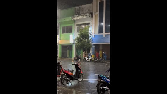 Man slips on wet road during rainfall in Surabaya, Indonesia