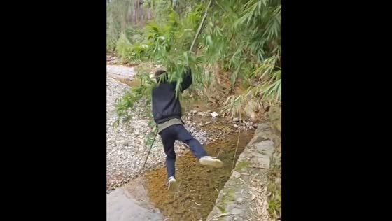 Person attempts to cross stream with bamboo twig in Sichuan province