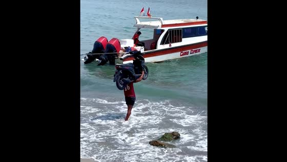Person carries motorcycle to a boat in Sanur, Bali