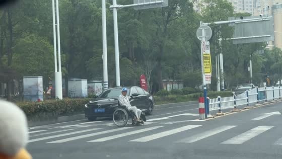 Old man in wheelchair crosses street at intersection in Jiangsu, China