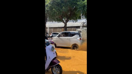 Mini EV pushes through muddy floodwater after water pipe burst in Guangxi, China