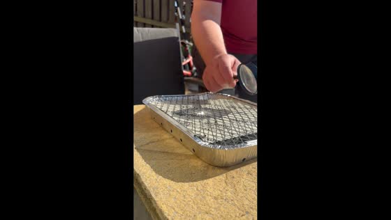 Dad starts BBQ with magnifying glass and sunlight in Motherwell, Scotland, UK