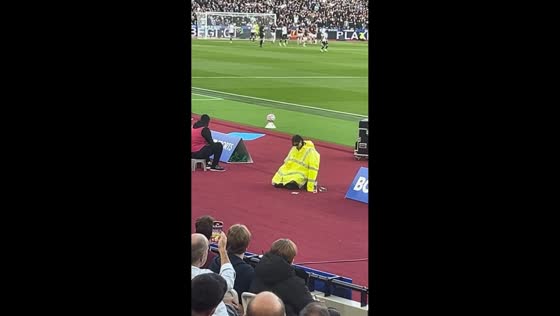 Woman in yellow raincoat rests beside football field in West Ham, England